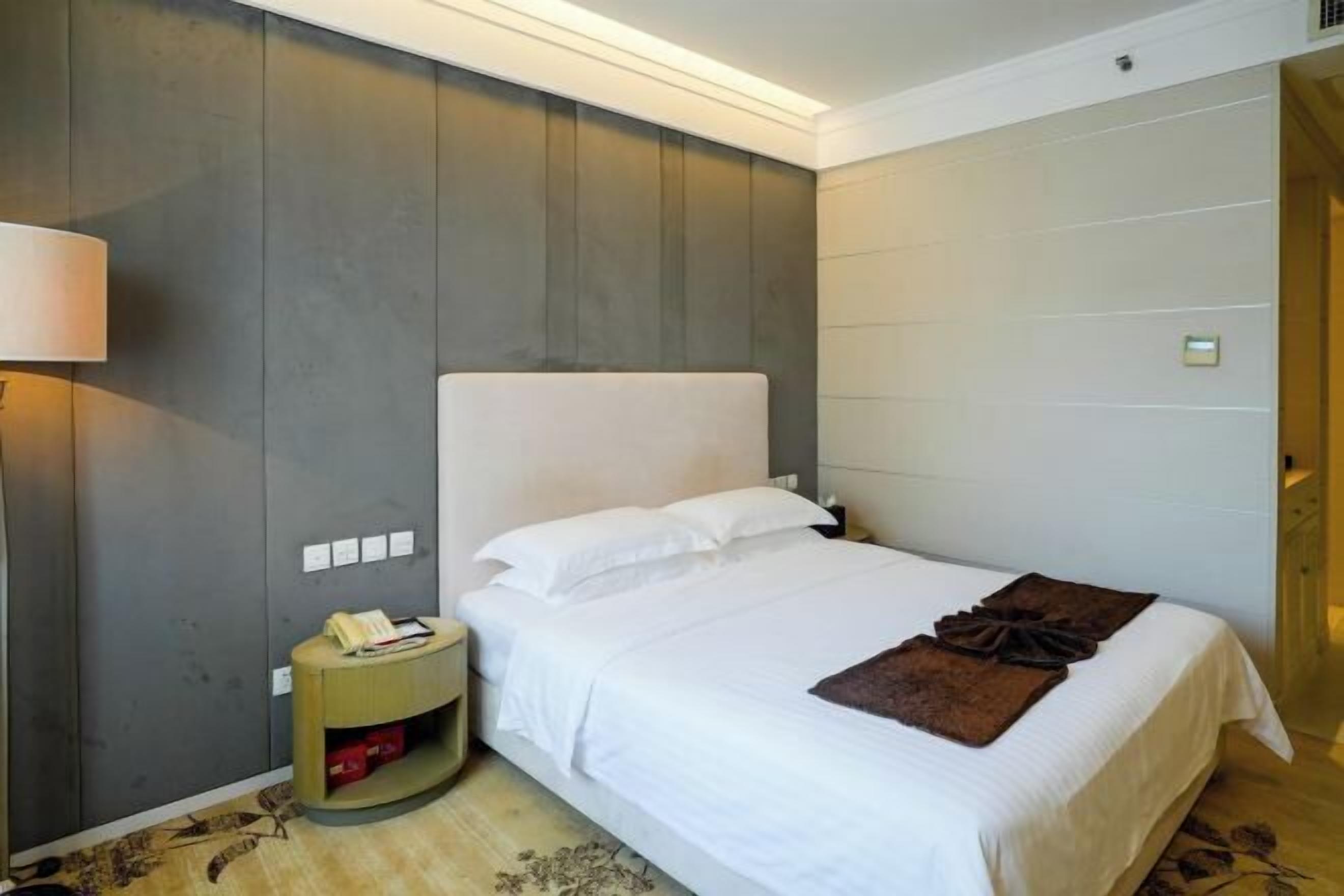 A hotel room with a bed, a nightstand, a lamp, and a wall-mounted phone.