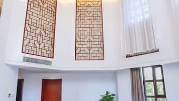 Een hotelkamer met een hoge plafond, een houten deur, een kamerplant en een raam met gordijnen.