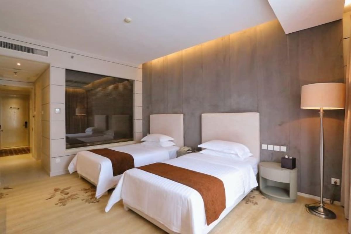 A hotel room with two beds, a mirror, a bedside table, and a floor lamp.