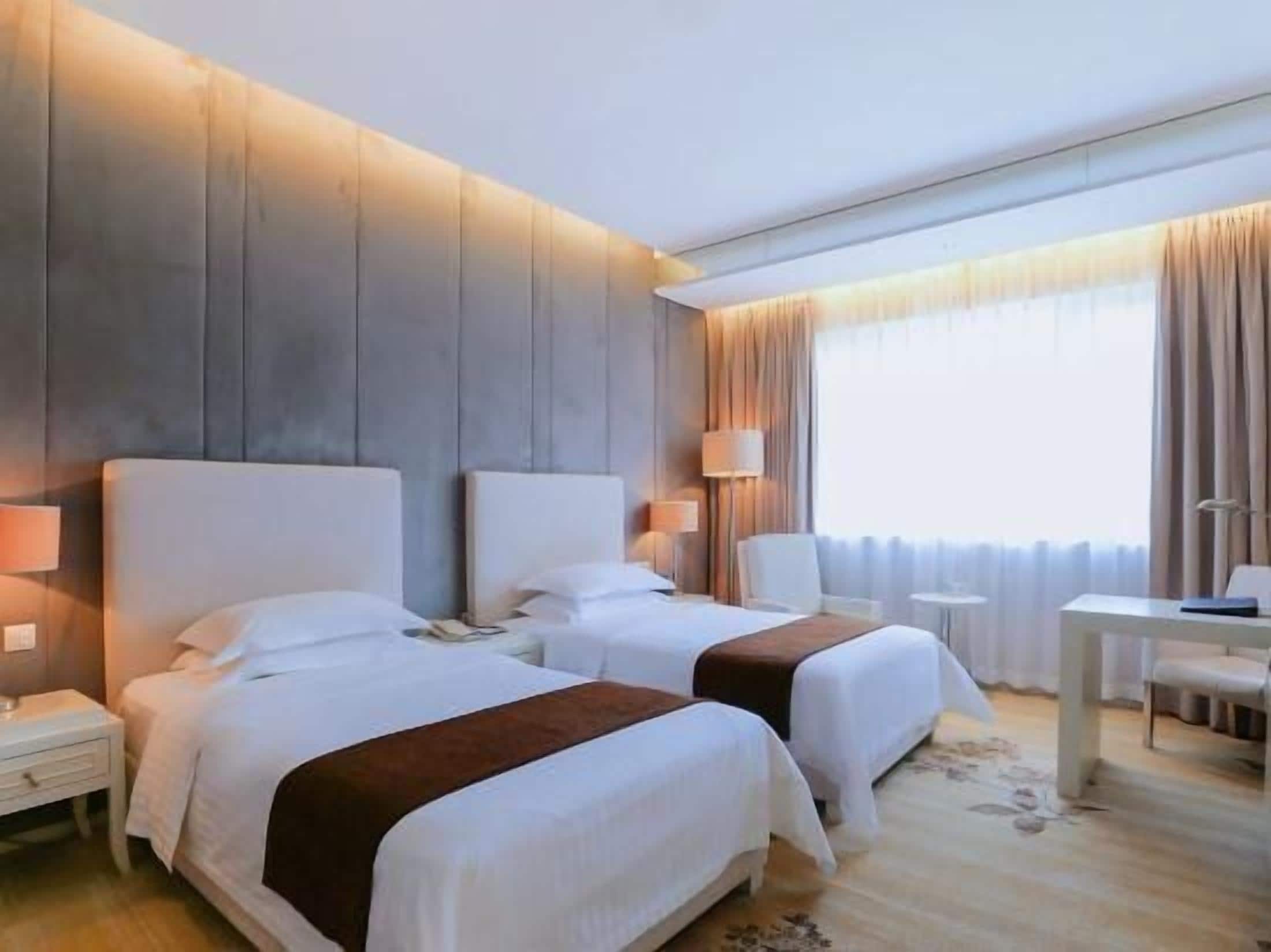 Habitación de hotel con dos camas, mesitas de noche, lámparas, un escritorio y una silla.