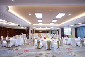 Un salón de banquetes con mesas redondas, manteles blancos y cintas doradas.
