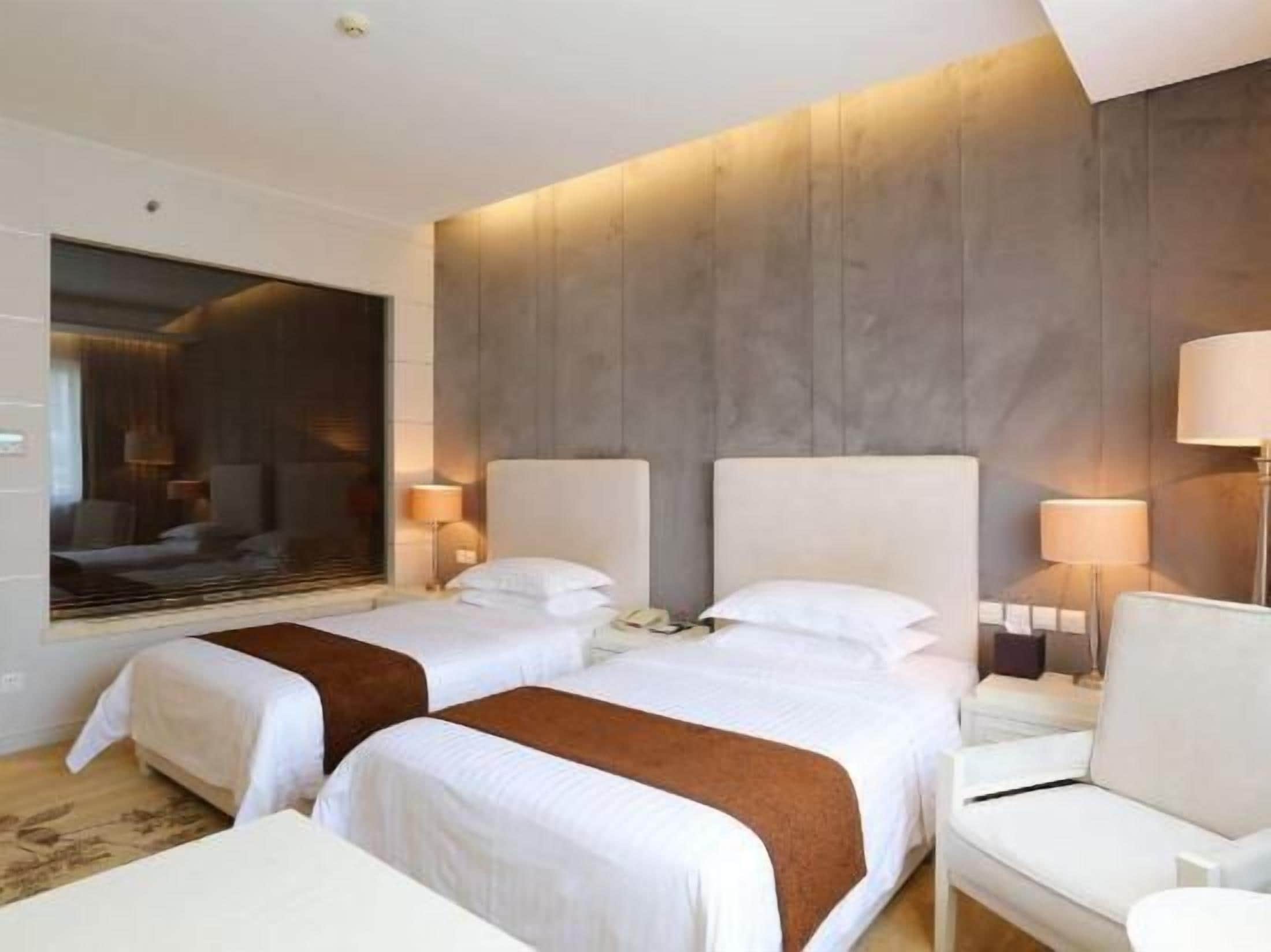 Habitación de hotel con dos camas, un sofá, un espejo grande y vista a la ciudad.