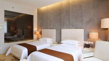Habitación de hotel con dos camas, un sofá, un espejo grande y vista a la ciudad.