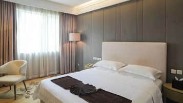 A hotel room with a large bed, a chair, a bedside table with a lamp, and a window with curtains.