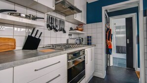 A modern kitchen with white cabinets, a gas stove, an oven, and a hanging rack with utensils. - Gateway to the Suffolk Coast (Kessingland)