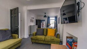 A compact living space with a sofa, a small table, a TV mounted on the wall, and a door leading to another room. - Gateway to the Suffolk Coast (Kessingland)