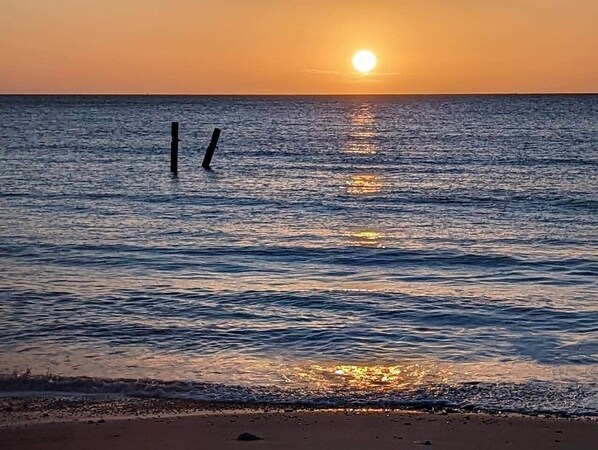 A sunset over a calm sea with a sandy beach.