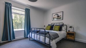 A bedroom with a bed, a nightstand, a lamp, and a window with curtains. - Gateway to the Suffolk Coast (Kessingland)