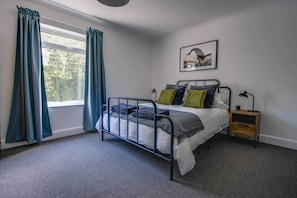 Un dormitorio con una cama, una mesita de noche, una lámpara y un ventanal con cortinas.