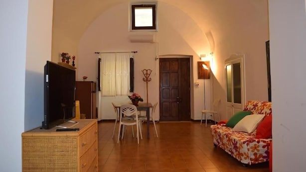 Un soggiorno accogliente con un divano, un tavolo da pranzo con sedie, una televisione su un comò e una piccola finestra.