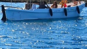 Una piccola imbarcazione con persone a bordo, una zona riparata e una costa rocciosa sullo sfondo.