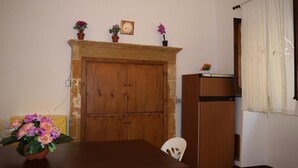 Una stanza con un armadio in legno, un tavolino con un vaso di fiori, una sedia bianca e un frigorifero.
