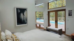 Une chambre dotée d’un grand lit, offrant une vue sur une piscine et comprenant un balcon avec une terrasse en bois.