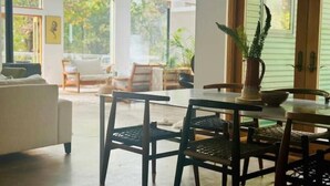 Un salon moderne avec un canapé, une table à manger et des chaises. De grandes fenêtres offrent une vue sur la verdure environnante.