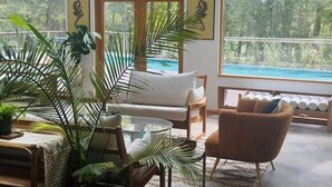 Un salon moderne avec un canapé, des fauteuils et une table basse, donnant sur une piscine.