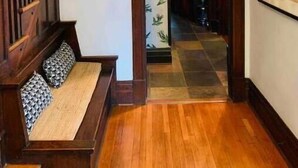 A wooden staircase leading to a second floor, a bench with patterned cushions, and a hallway with a tiled floor and a door leading to a kitchen area. - 1905 Tudor Revival house in Historic Shaw (St. Louis)