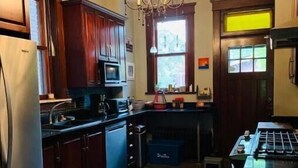 A kitchen with dark wooden cabinets, stainless steel appliances, a chandelier, and a window providing natural light. - 1905 Tudor Revival house in Historic Shaw (St. Louis)