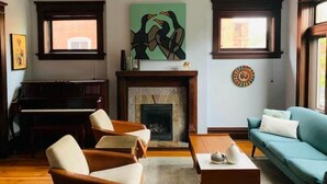 A living room with a fireplace, a piano, and a sofa. - 1905 Tudor Revival house in Historic Shaw (St. Louis)