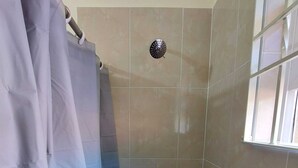 Une douche avec une porte en verre, un pommeau de douche et un robinet de réglage.