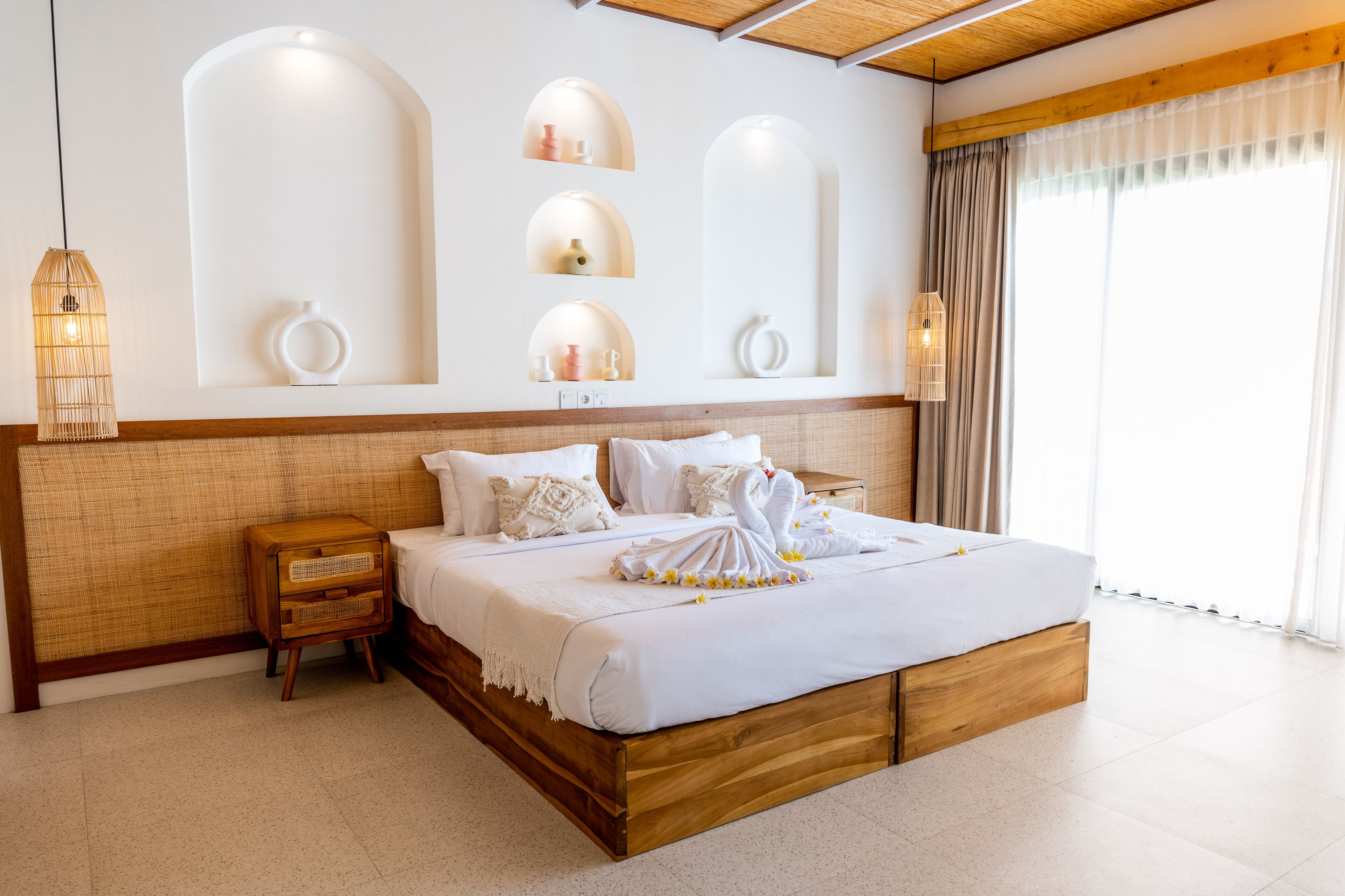 Um quarto espaçoso com uma cama grande, cabeceira de madeira e prateleiras embutidas decoradas com objetos.