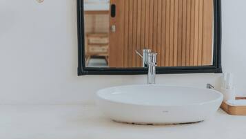 Un baño con un lavamanos blanco, un espejo con marco negro y cestas tejidas en la estantería.