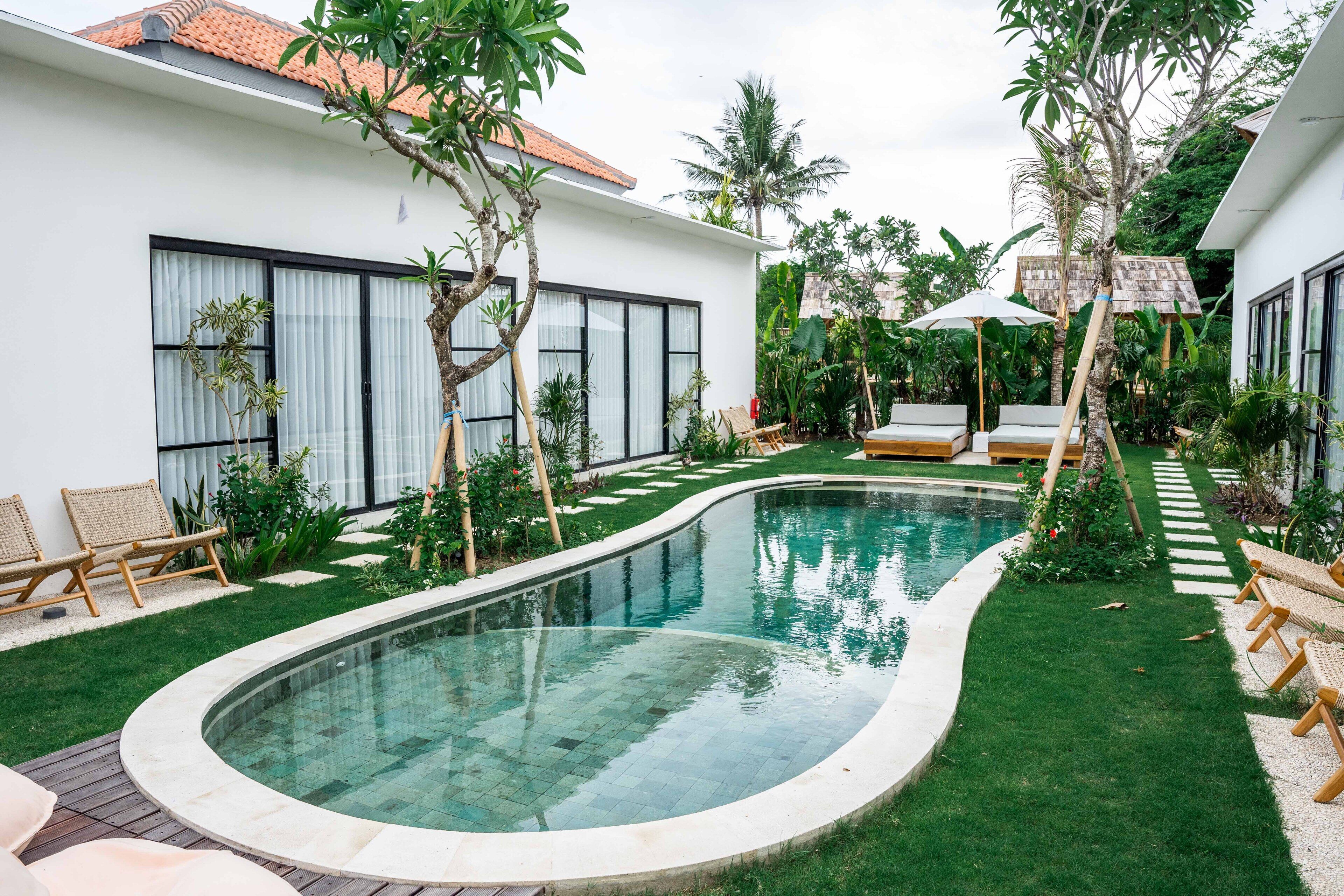 Uma casa moderna com piscina, rodeada por vegetação exuberante e mobiliário de exterior.