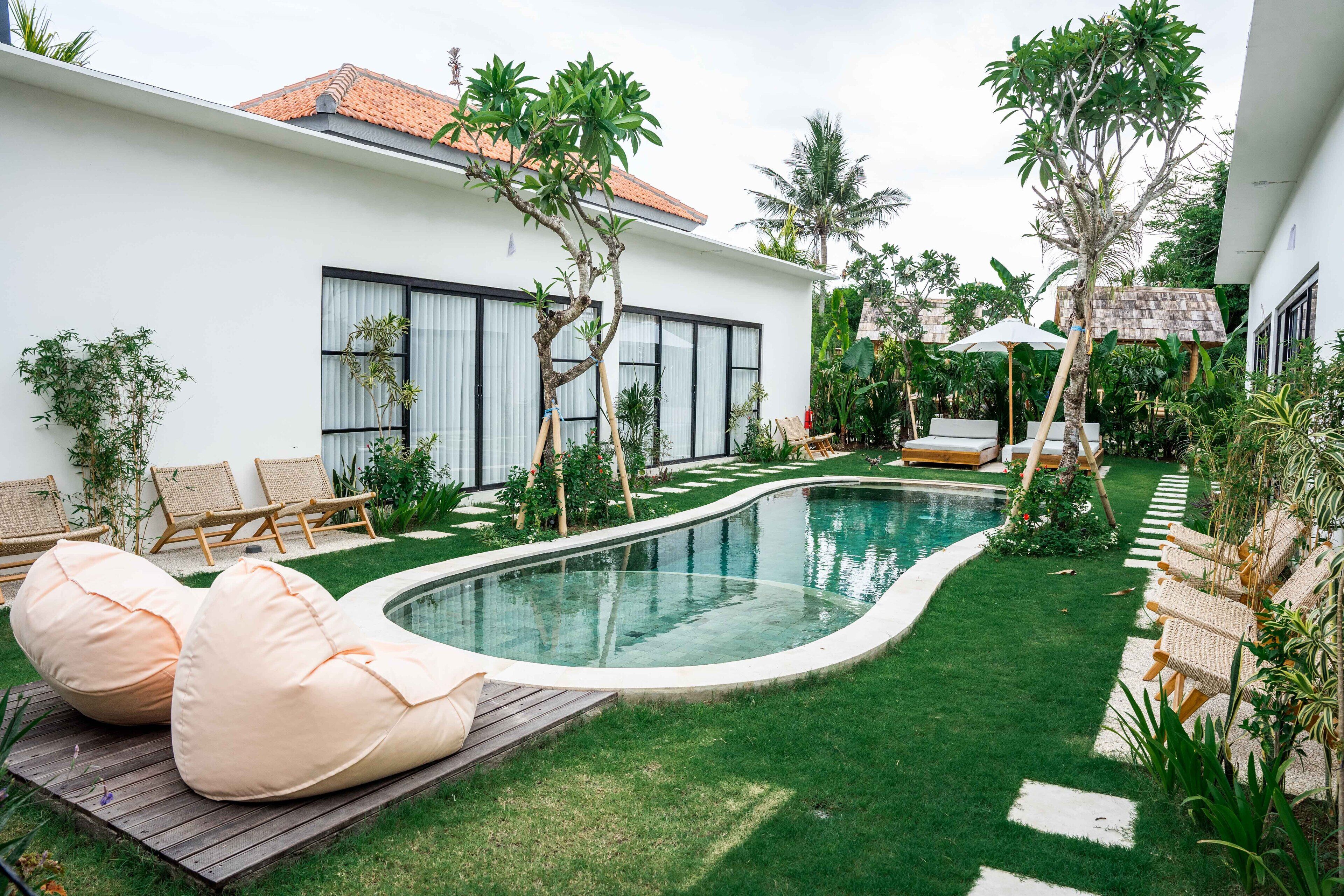 Un espace piscine extérieur moderne, doté d’une piscine aux lignes courbes, de chaises longues et d’une pelouse bien entretenue.