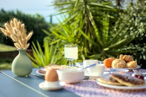 A table set outdoors with a variety of breakfast items including croissants, eggs, and a glass of juice. - Villa Morro Suites (Morrovalle)