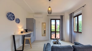 A modern living room with a sofa, a coffee table, and a dining area with a table and chairs. There is a large window with curtains and a view of the outdoors. - Villa Morro Suites (Morrovalle)