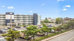 Een hotel met meerdere verdiepingen, een parkeerplaats, verschillende bomen en een heldere lucht.