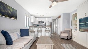 Een moderne woonkamer met een bank, salontafel en stoelen. Achtergrond: een keuken met een eethoek.