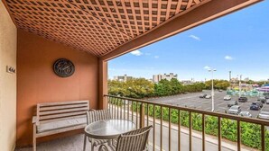Een balkon met een houten bankje en een tafel, met uitzicht op een parkeerplaats en stadsbeeld.