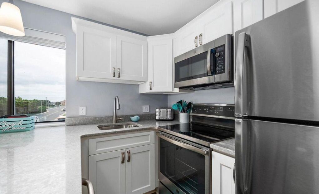 A modern kitchen with white cabinets, stainless steel appliances, and a window providing a view of the outside.