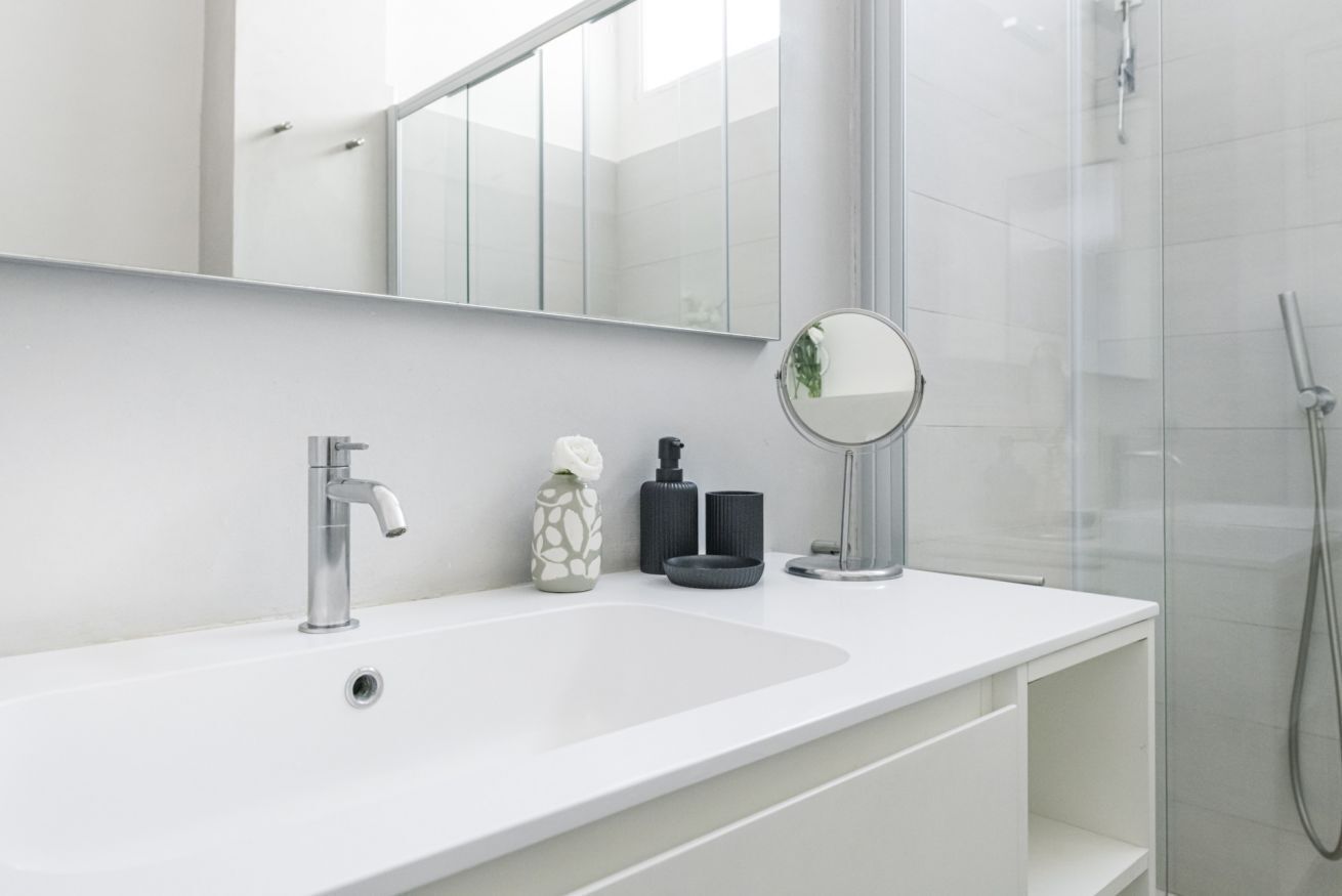 A modern bathroom with a white sink, a mirror, and a glass shower enclosure.