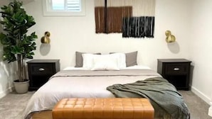Una camera da letto con un letto, due comodini, una panca, una pianta in vaso e una finestra.