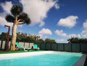 En swimmingpool med solstolar, en palm och en klarblå himmel.