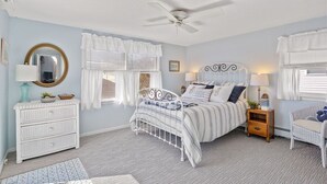 Une chambre à coucher comprenant un lit, des tables de chevet, une commode, un miroir et un ventilateur de plafond.