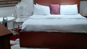 Hotellihuone, jossa on puinen sängynpääty, valkoinen sänky, jossa on kaksi tyynyä, punainen matto, valkoinen tuoli ja pieni pyöreä pöytä.