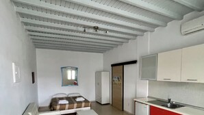 A room with a sofa, a small table, a kitchenette with red cabinets, and a ceiling with exposed beams.