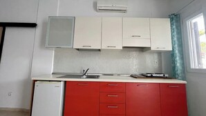 A kitchen with white upper cabinets, a red lower cabinet, a white refrigerator, and a window with a curtain.