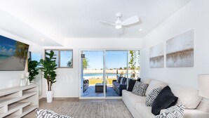 A modern living room with a large window, a ceiling fan, and a view of the beach. - Modern Beachfront Retreat 2 King Suites + (Puerto Peñasco)