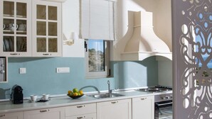 Una cocina con armarios blancos, una ventana con persianas, una estufa y un lavabo.
