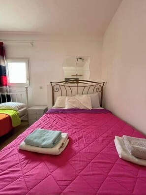A bedroom with a bed, a nightstand, a mirror, and a window.