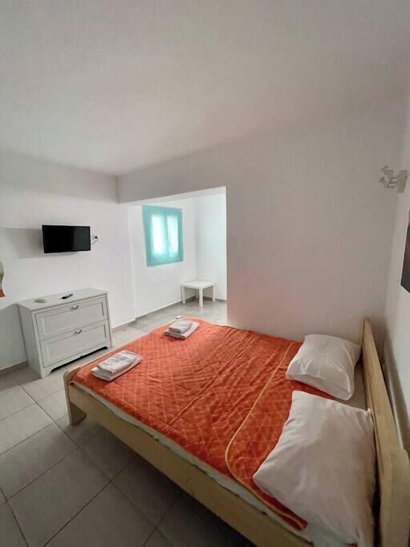 A bedroom with a bed, a nightstand, a TV, and a window.