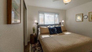 A bedroom with a bed, a ceiling fan, a window with blinds, and a small side table with a plant. - NEW, Stunning Flagstaff Home w/ Deck and Firepit (Flagstaff)