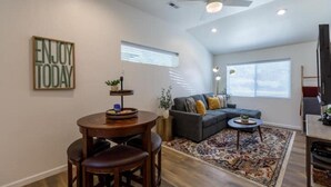 A modern living room with a gray sofa, a coffee table, and a dining area with a round table and bar stools. - NEW, Stunning Flagstaff Home w/ Deck and Firepit (Flagstaff)