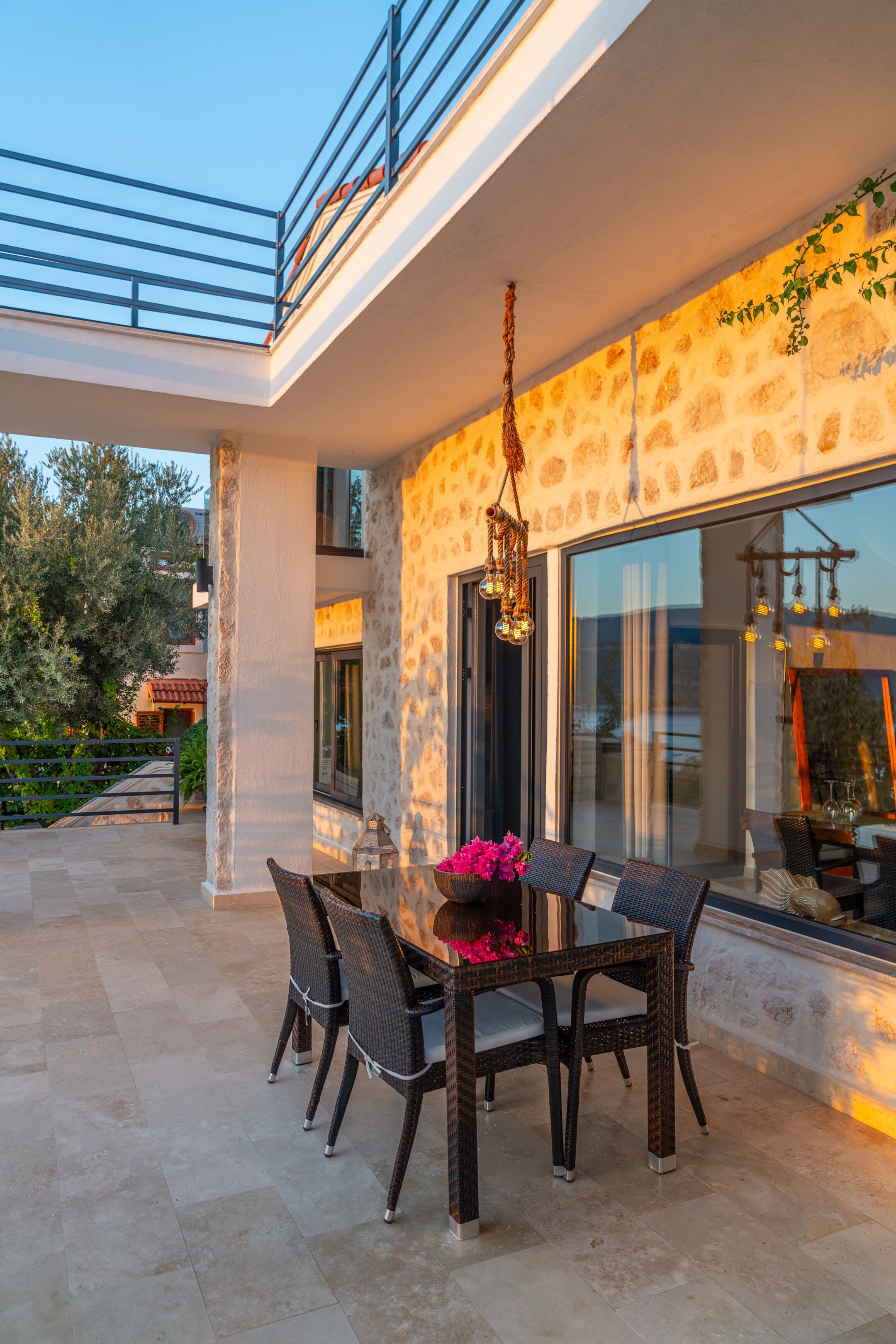 An outdoor patio with a dining table and chairs, a hanging light fixture, and a stone wall.