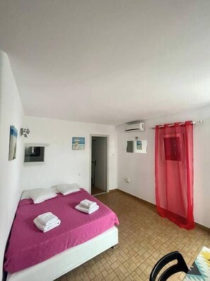 A bedroom with a bed, a red canopy, a white wall, and a tiled floor.