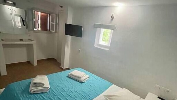 A room with a bed, a desk, a small window, and a wall-mounted TV. - Two-room apartment for 4 people, with (Mikonos)