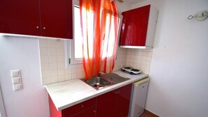 Una cocina compacta con gabinetes rojos, una encimera blanca, un fregadero y un lavavajillas pequeño.